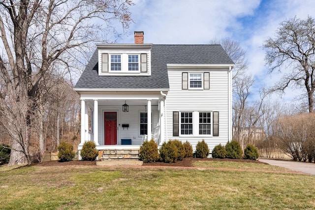 view of front of property featuring a chimney, roof with shingles, covered porch, and a front yard