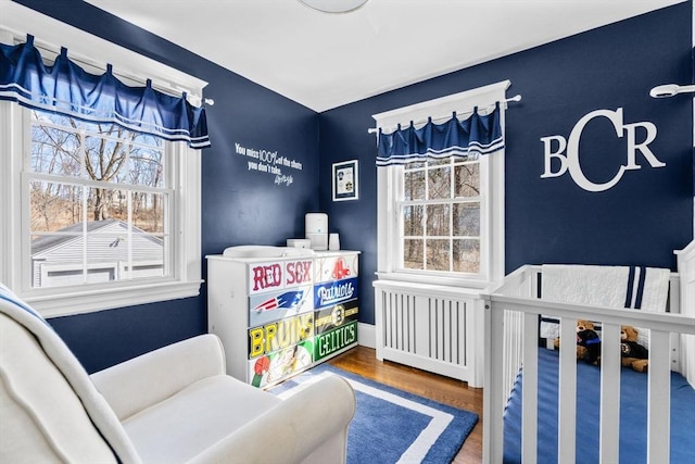 bedroom featuring a crib, wood finished floors, and radiator heating unit