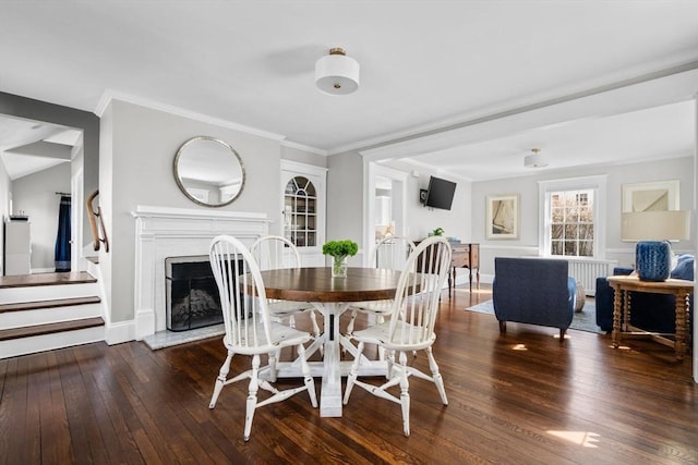 dining area featuring a fireplace with raised hearth, baseboards, ornamental molding, and hardwood / wood-style floors