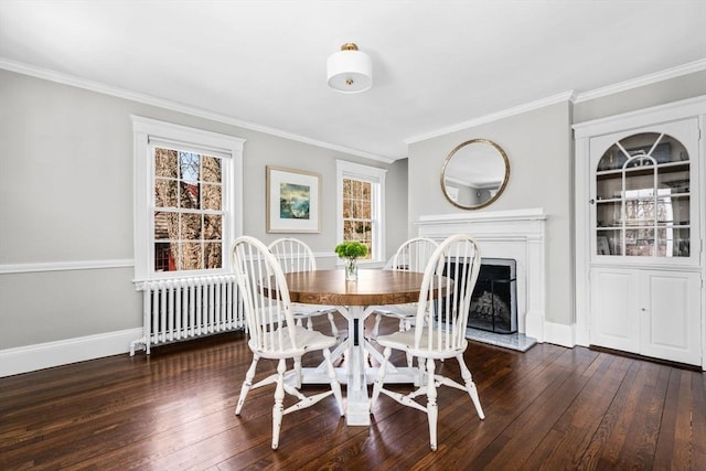 dining room featuring baseboards, radiator heating unit, a fireplace with raised hearth, dark wood-style flooring, and crown molding