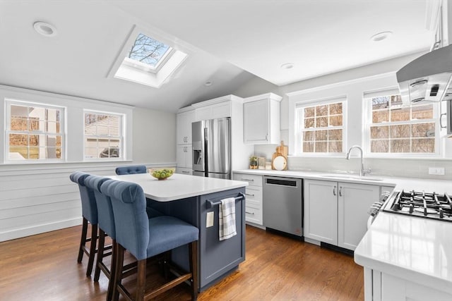 kitchen with dark wood-type flooring, a breakfast bar area, light countertops, appliances with stainless steel finishes, and a sink