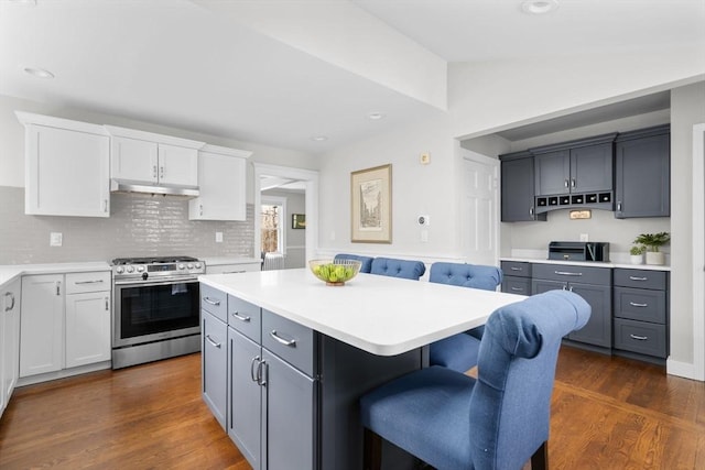 kitchen with under cabinet range hood, stainless steel range with gas stovetop, a breakfast bar area, and dark wood-style floors