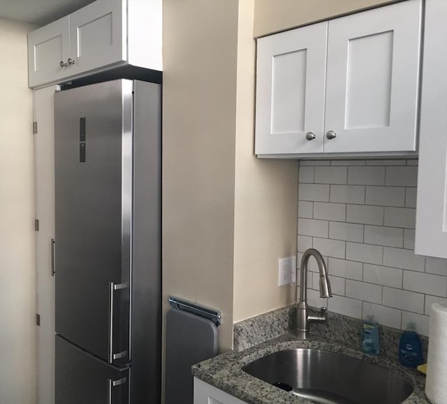 kitchen featuring stainless steel refrigerator, tasteful backsplash, white cabinetry, sink, and dark stone countertops