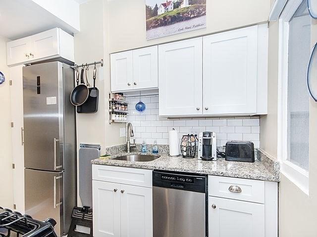 kitchen featuring sink, white cabinets, backsplash, stainless steel appliances, and light stone countertops