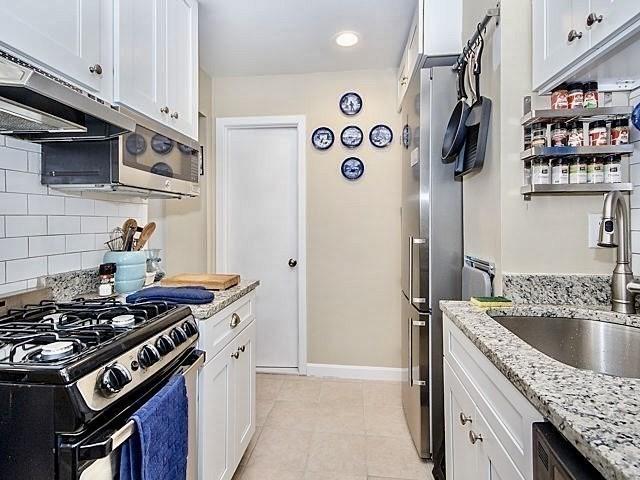 kitchen with white cabinetry, sink, exhaust hood, light stone counters, and stainless steel appliances