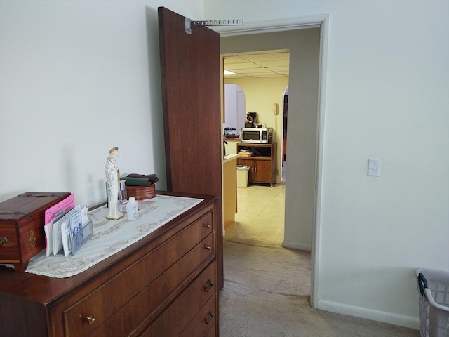 hallway featuring a paneled ceiling, baseboards, arched walkways, and light colored carpet