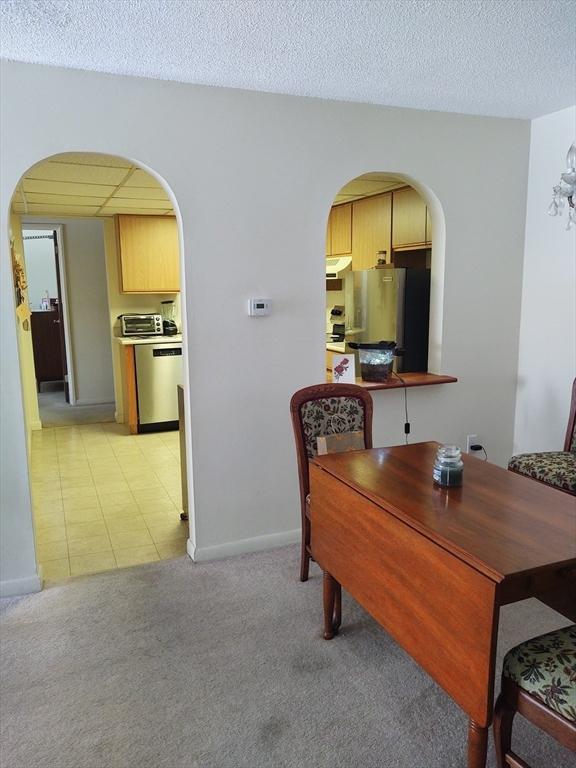 dining space featuring arched walkways, light carpet, a textured ceiling, and baseboards