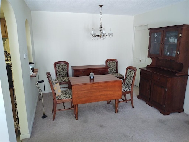 dining room featuring arched walkways, light carpet, a notable chandelier, and baseboards