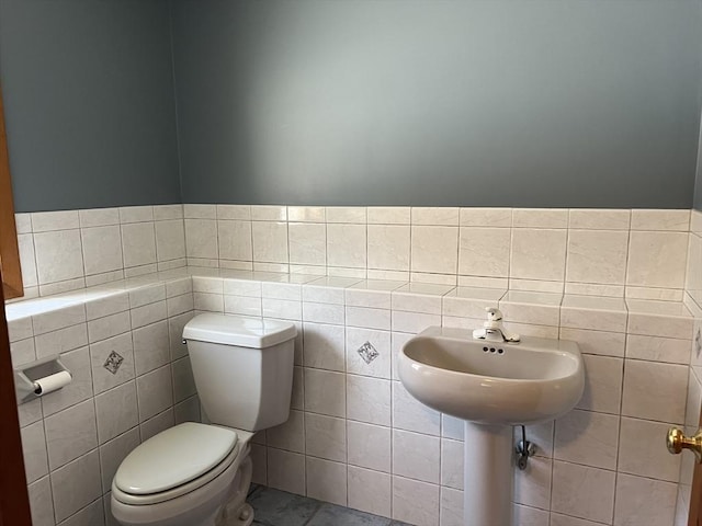 bathroom with a wainscoted wall, toilet, and tile walls