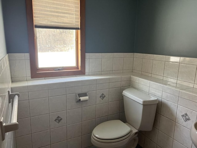 bathroom with toilet, a wainscoted wall, and tile walls