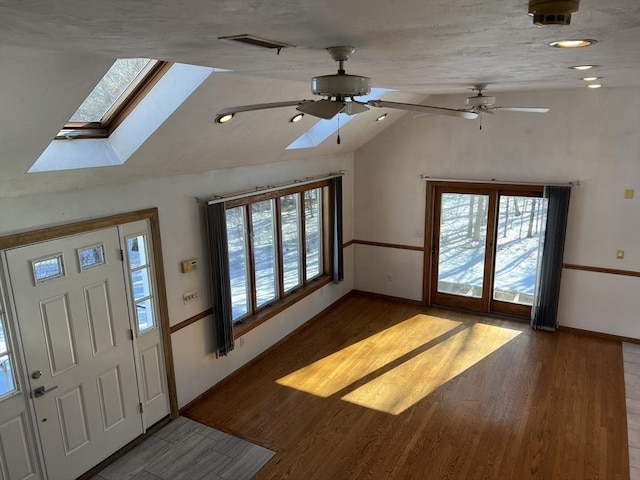 foyer entrance with visible vents, ceiling fan, wood finished floors, vaulted ceiling with skylight, and baseboards