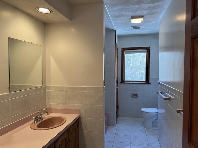 full bathroom featuring visible vents, toilet, tile patterned floors, vanity, and tile walls