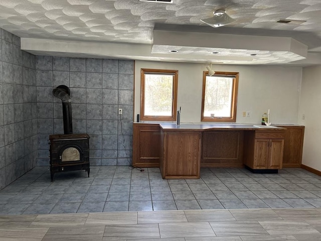 interior space with a wood stove, light tile patterned floors, visible vents, and a textured ceiling