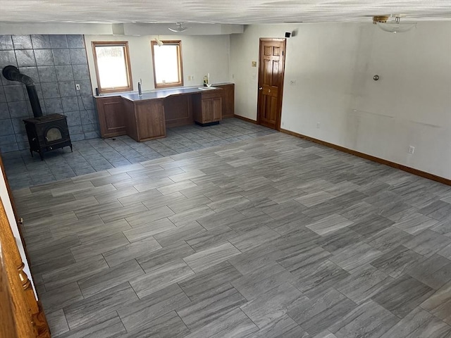 kitchen with a wood stove, baseboards, brown cabinetry, and a sink