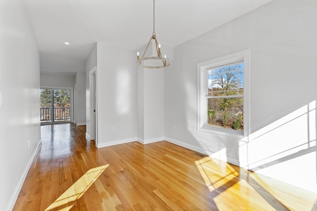 unfurnished dining area with wood-type flooring, a healthy amount of sunlight, and a chandelier