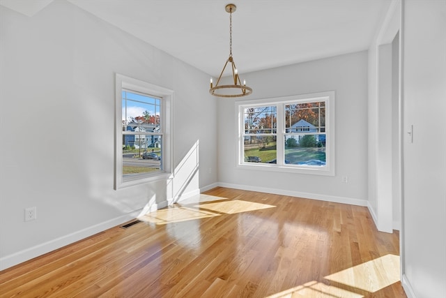 unfurnished dining area with a healthy amount of sunlight, light wood-type flooring, and a notable chandelier