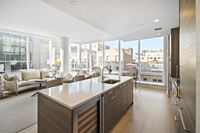 kitchen featuring visible vents, wine cooler, dark brown cabinetry, wood finished floors, and a sink