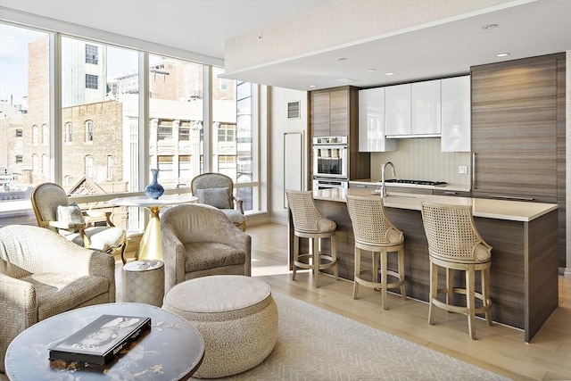 kitchen with a wall of windows, a center island with sink, light countertops, a kitchen breakfast bar, and modern cabinets