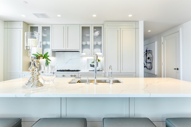 kitchen featuring backsplash, sink, light stone counters, and a breakfast bar area