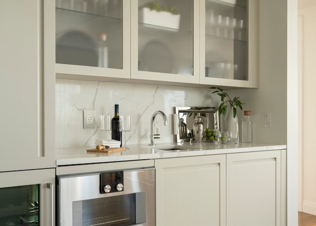 bar with white cabinetry, decorative backsplash, sink, and beverage cooler