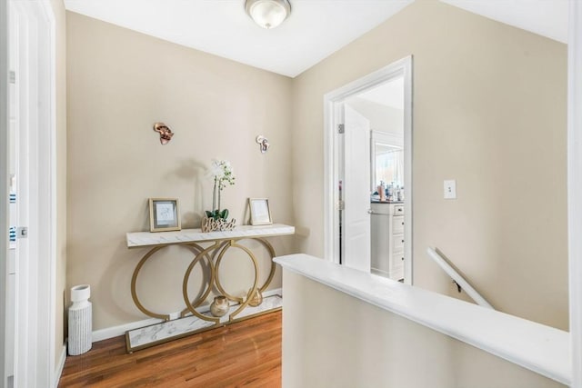 hallway featuring baseboards, wood finished floors, and an upstairs landing