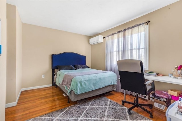 bedroom with wood finished floors, baseboards, and a wall mounted AC