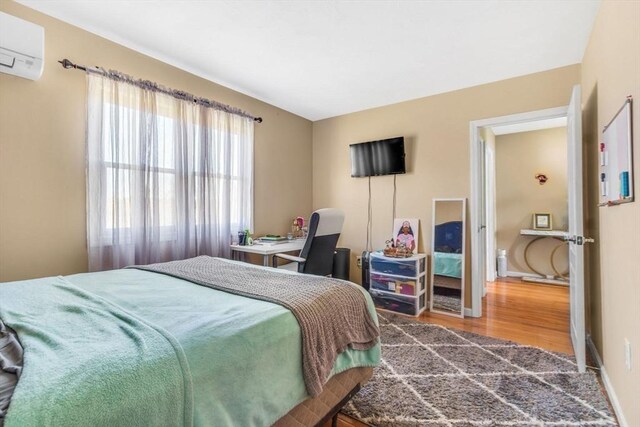 bedroom with baseboards, an AC wall unit, and wood finished floors