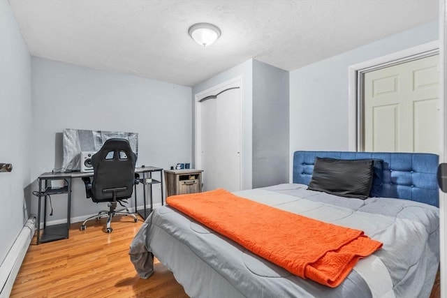 bedroom featuring a closet, a baseboard radiator, baseboards, and wood finished floors