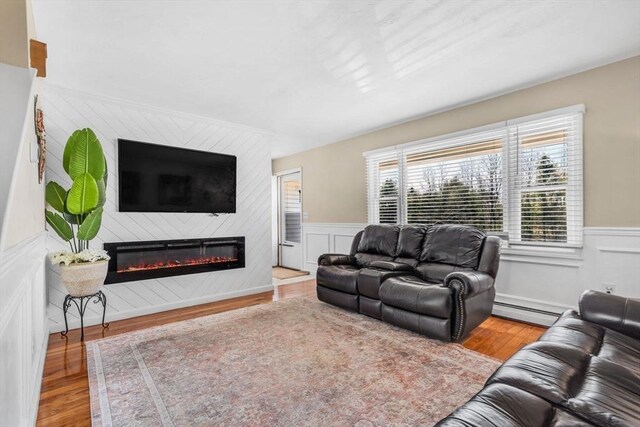 living room with a large fireplace, baseboard heating, wainscoting, and wood finished floors