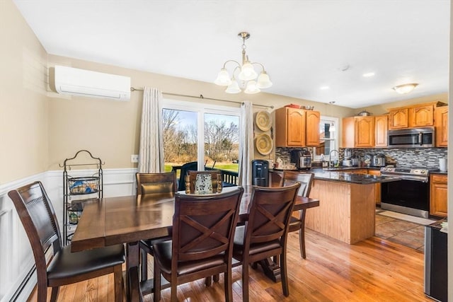 dining space with light wood-type flooring, a wall mounted air conditioner, a wainscoted wall, and a chandelier