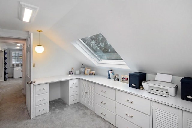 home office with light carpet, vaulted ceiling with skylight, and built in desk