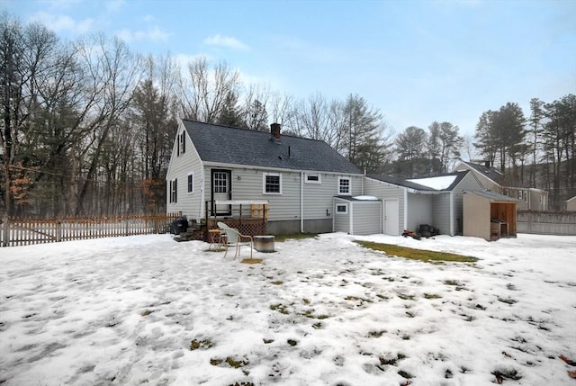 snow covered property featuring a detached garage, a storage shed, fence, an outdoor structure, and a wooden deck