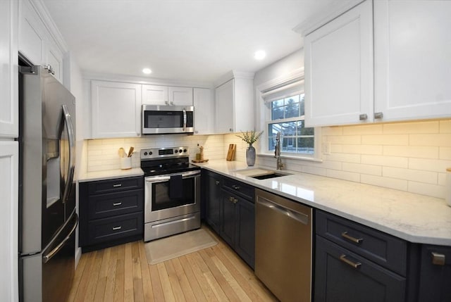 kitchen with light wood-type flooring, white cabinetry, stainless steel appliances, and a sink