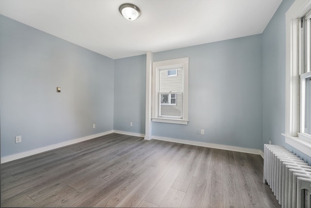 spare room featuring wood-type flooring, radiator heating unit, and plenty of natural light