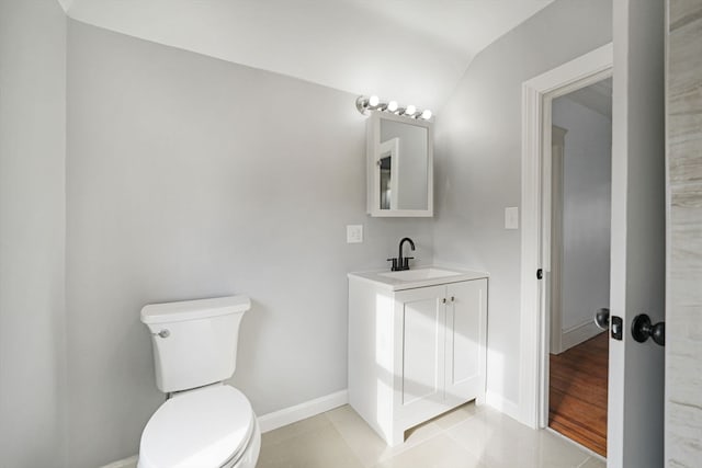 bathroom with toilet, vanity, vaulted ceiling, and tile patterned flooring