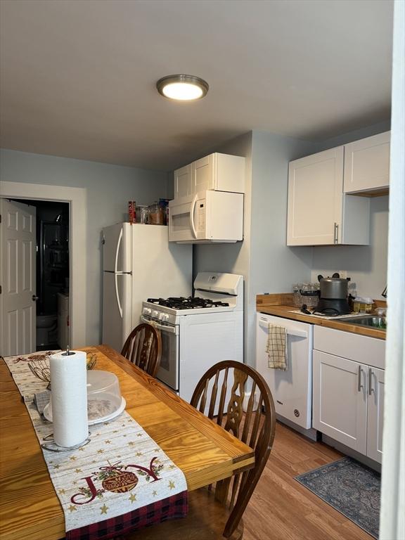 kitchen with light wood-type flooring, white cabinets, and white appliances