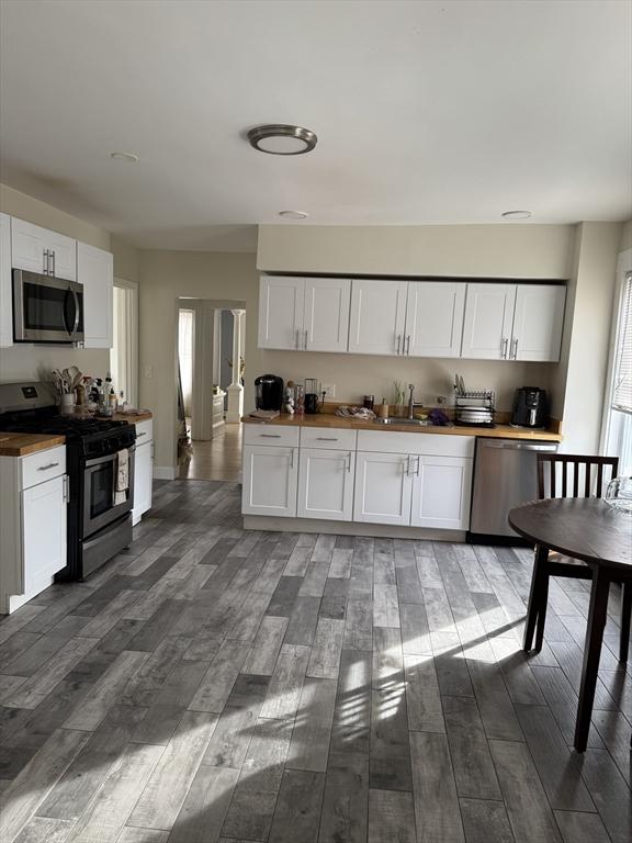 kitchen featuring appliances with stainless steel finishes, wood counters, sink, white cabinets, and dark hardwood / wood-style flooring