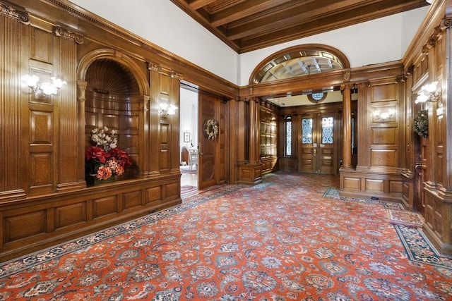 foyer entrance with ornate columns, wooden walls, a towering ceiling, and ornamental molding