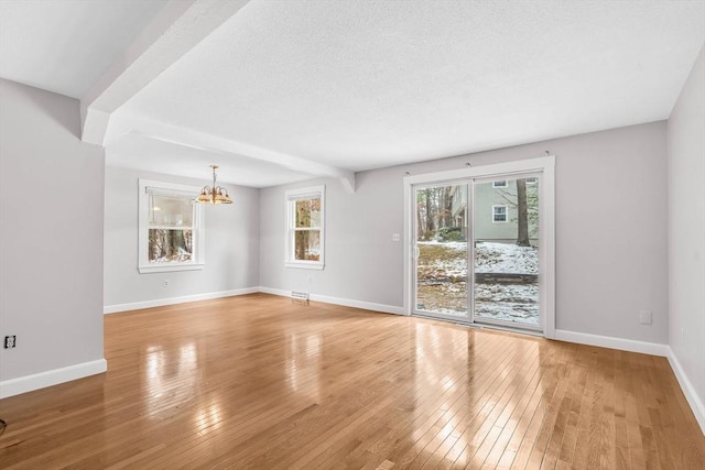 unfurnished living room with light wood-style flooring, a textured ceiling, baseboards, and an inviting chandelier