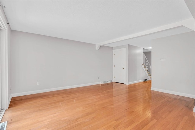 unfurnished room featuring light wood-type flooring, baseboards, visible vents, and stairs