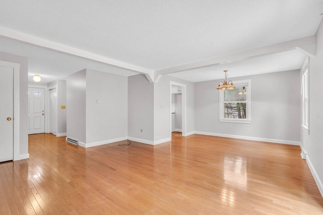 spare room featuring a notable chandelier, a textured ceiling, baseboards, and light wood-style floors