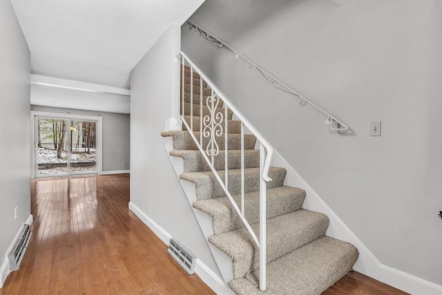 stairs with visible vents, baseboard heating, baseboards, and hardwood / wood-style flooring