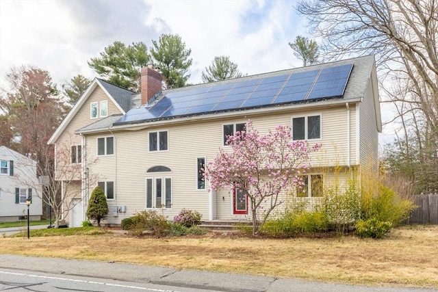 view of front of home with fence, a chimney, roof with shingles, and solar panels