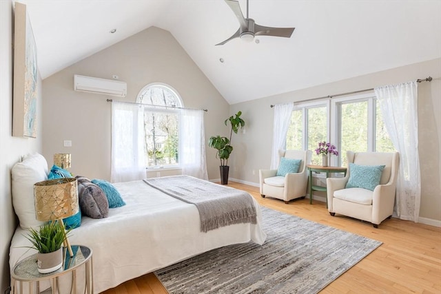 bedroom featuring light wood finished floors, a ceiling fan, baseboards, a wall mounted AC, and high vaulted ceiling