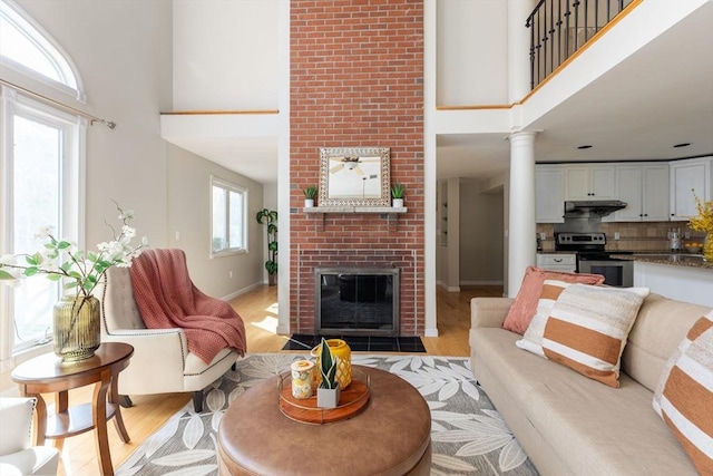 living room featuring baseboards, light wood-style flooring, a towering ceiling, and a fireplace