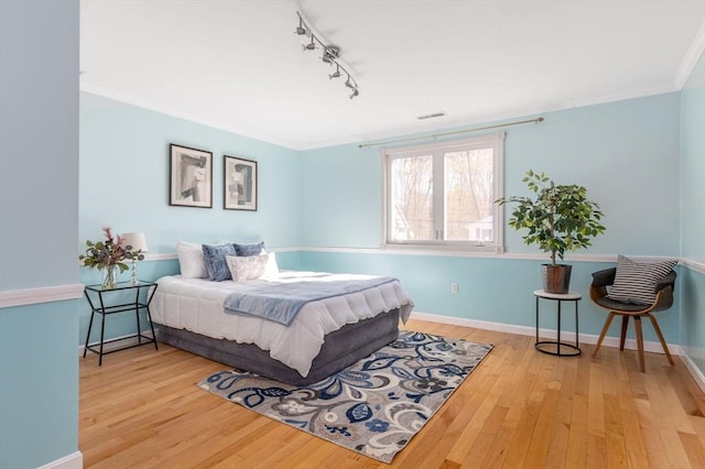 bedroom featuring hardwood / wood-style flooring, baseboards, visible vents, track lighting, and ornamental molding