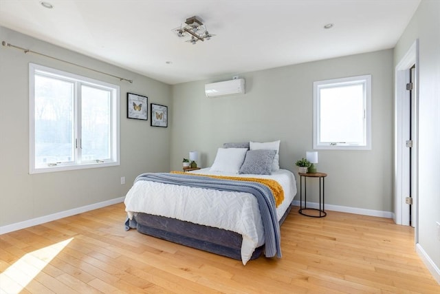 bedroom featuring light wood finished floors, multiple windows, and a wall mounted AC