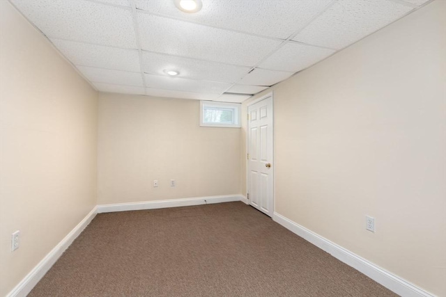 below grade area with dark colored carpet, baseboards, and a paneled ceiling