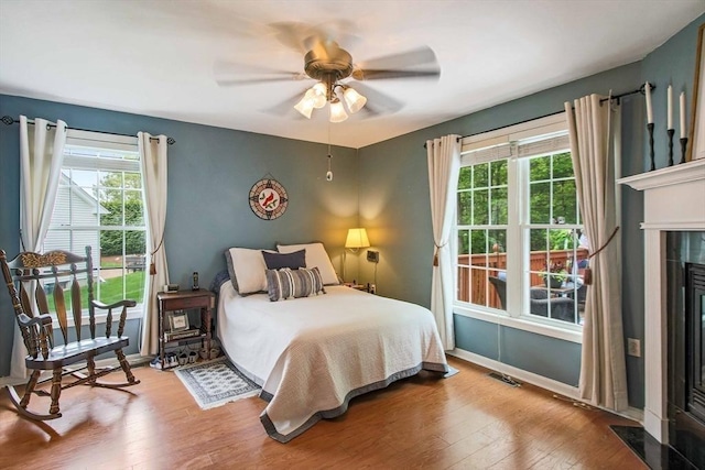 bedroom featuring multiple windows, wood finished floors, a fireplace, and baseboards