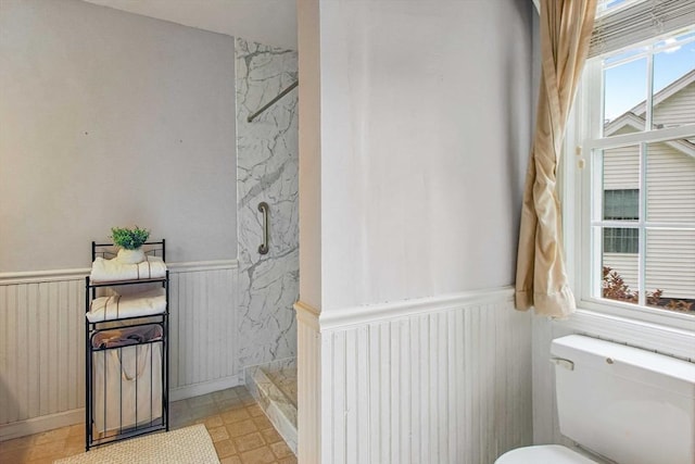 bathroom featuring a wainscoted wall, a marble finish shower, and toilet